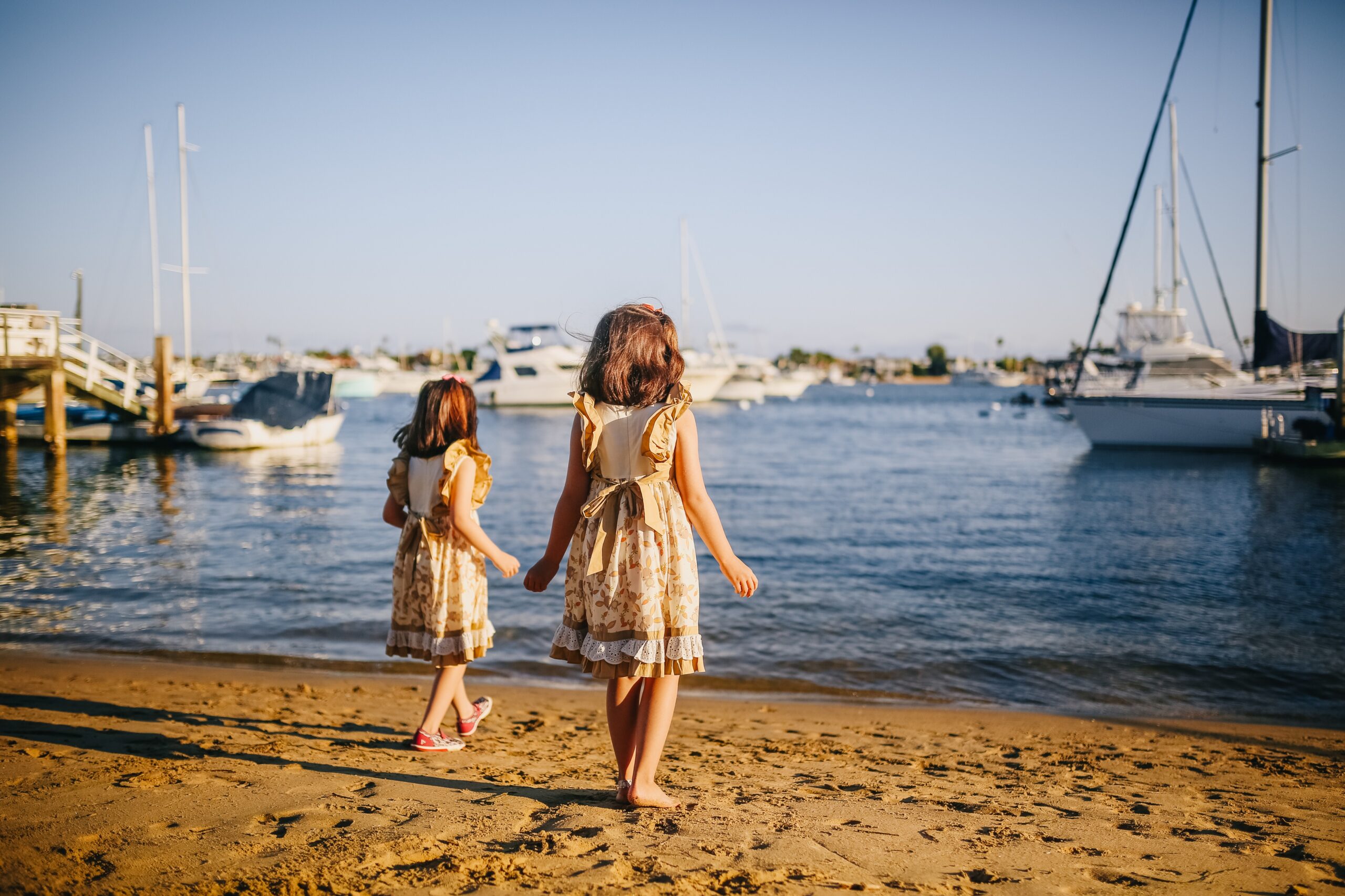 Twin girls stand on the shore with boats in the distance